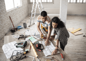 couple working on plans for a home remodel with tools laid out on a table and a ladder in the background